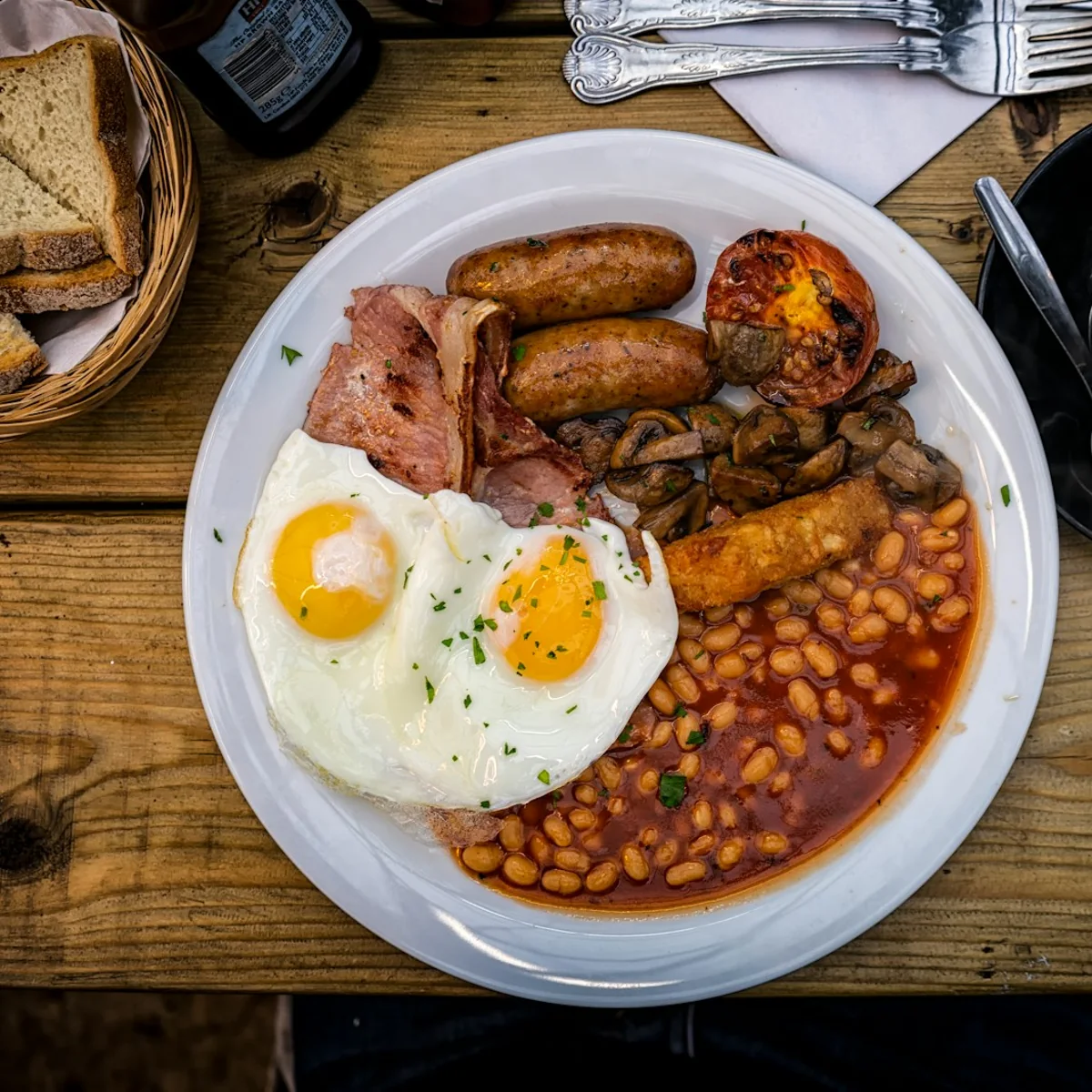 A full English breakfast with two fried eggs, bacon, sausages, mushrooms and beans, with a flat white on the side