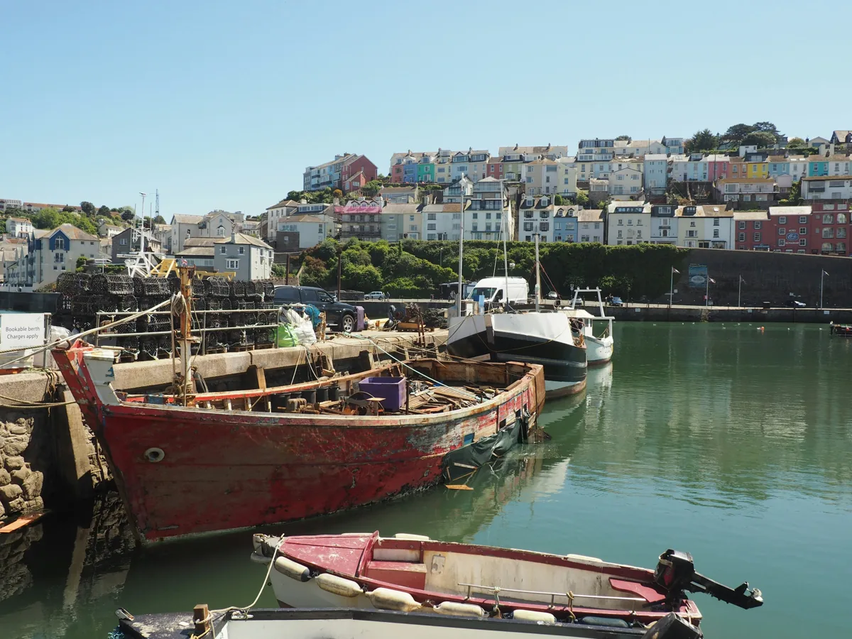 Fishing boats in a harbour below rows of colourful houses on the hillside