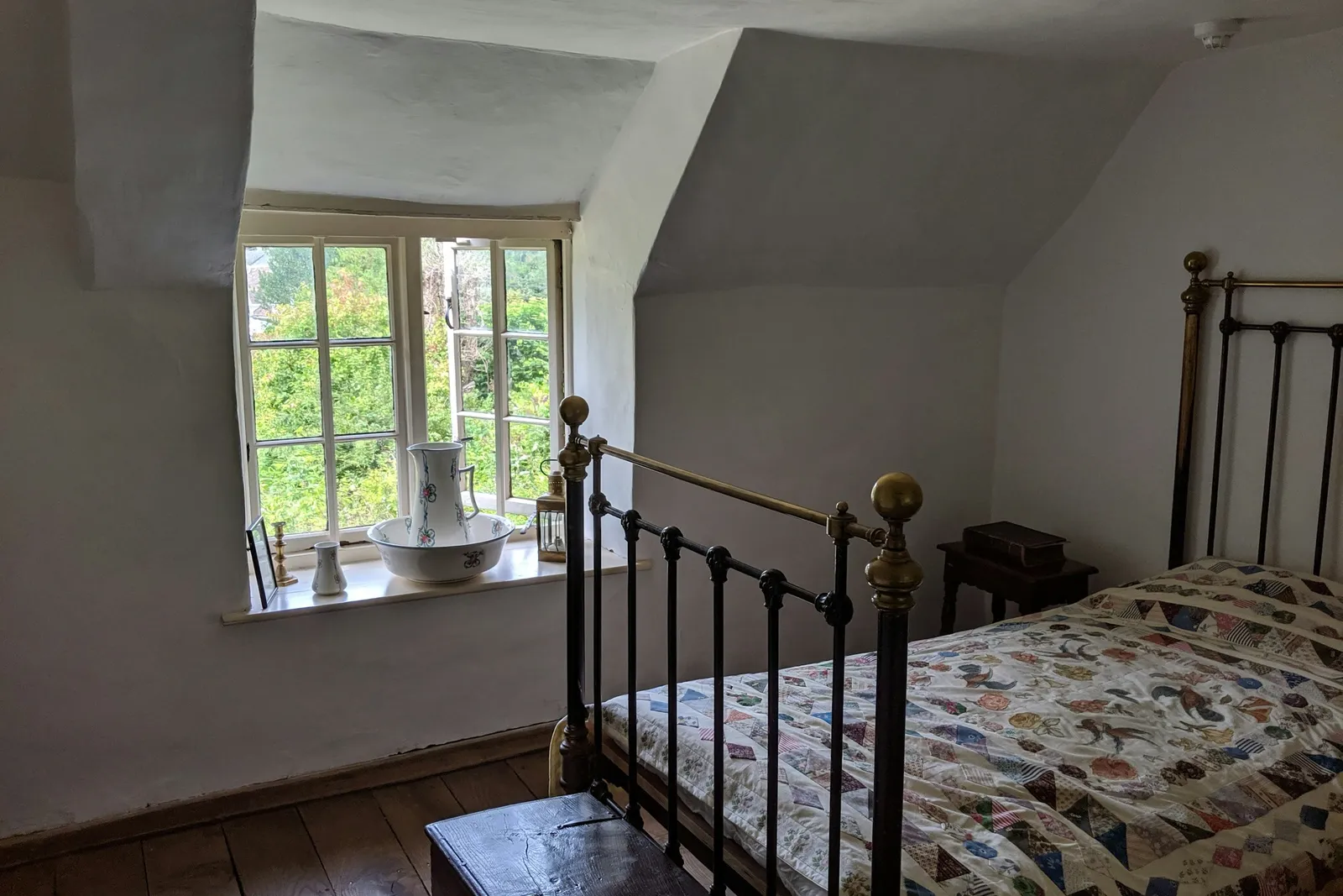 Brass bed and a cottage window open onto a green garden